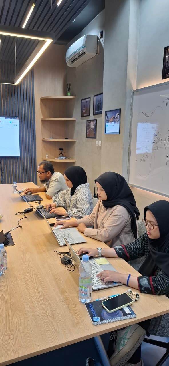 Casakha team members working on laptops during an Odoo implementation workshop, with a Casakha-branded notebook in the foreground